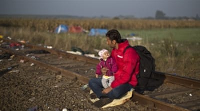 An Afghan refugee holding his child rests on a railway track after crossing the Serbia-Hungary border [AP]