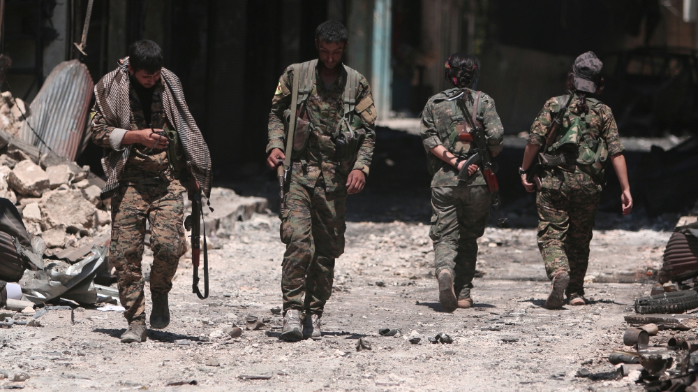 Syria Democratic Forces (SDF) fighters walk on the rubble of damaged shops and buildings in the city of Manbij