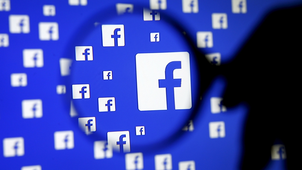 A man poses with a magnifier in front of a Facebook logo on display in this illustration taken in Sarajevo