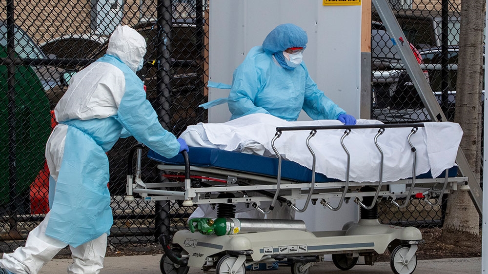 Medical personnel wearing personal protective equipment remove a body from the Wyckoff Heights Medical Center to refrigerated containers parked outside in the Brooklyn borough of New York