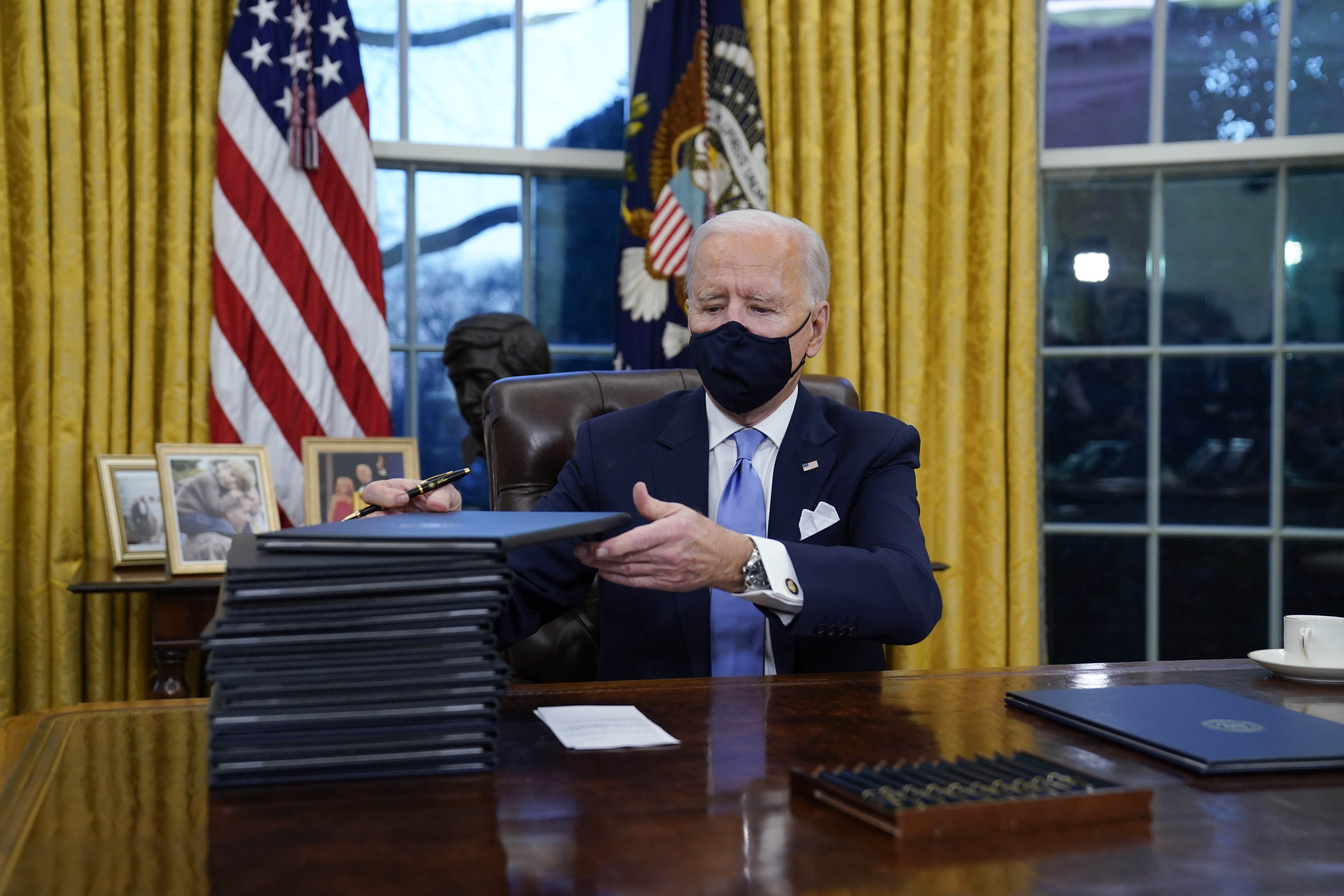 In this January 20, 2021, file photo, President Joe Biden signs his first executive orders in the Oval Office of the White House in Washington, DC. Six of Biden's 17 first-day executive orders dealt with immigration, such as halting work on a border wall in Mexico and lifting a travel ban on people from several predominantly Muslim countries [File: AP Photo/Evan Vucci]