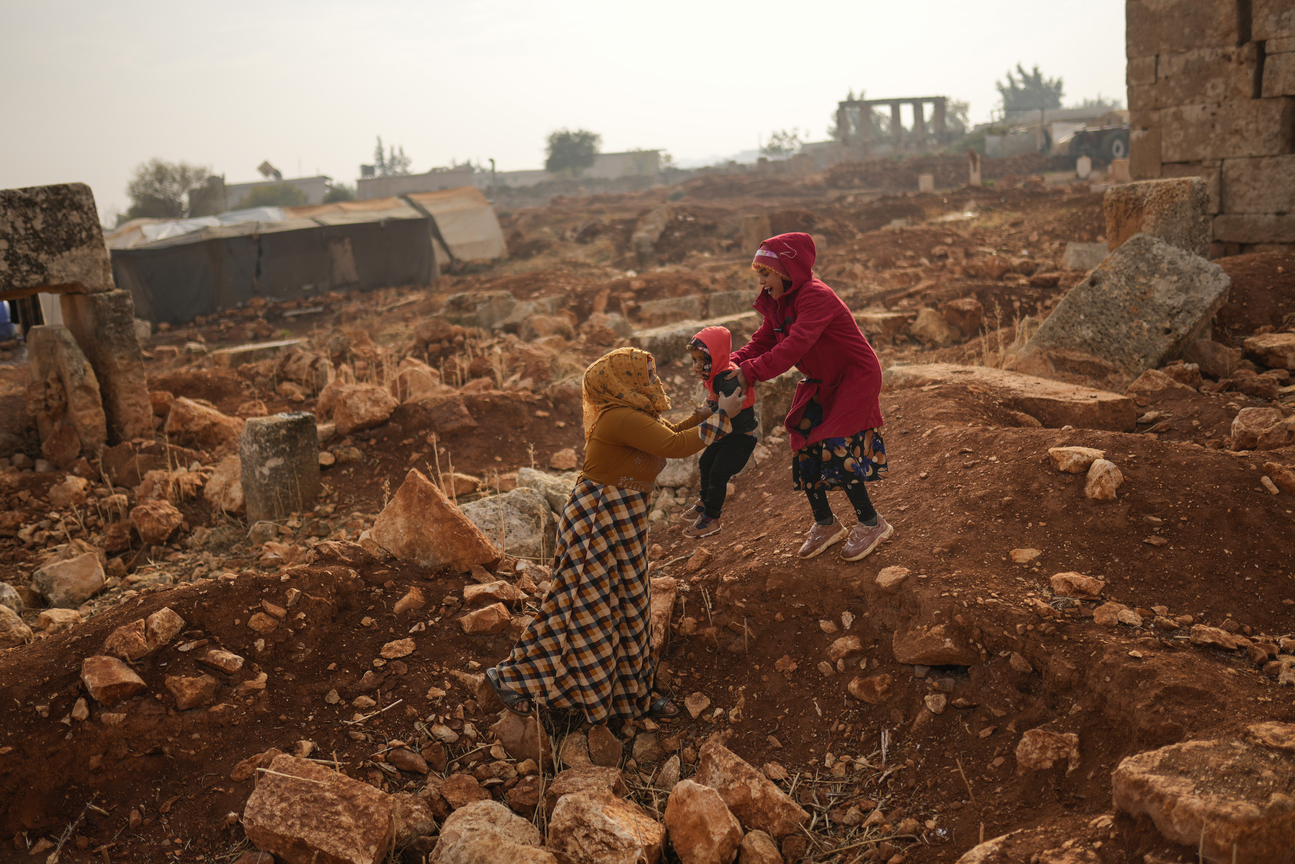 A Syrian woman holds a child next to ancient Roman era ruins where they have set their tents in Sarmada district, north of Idlib city, Syria