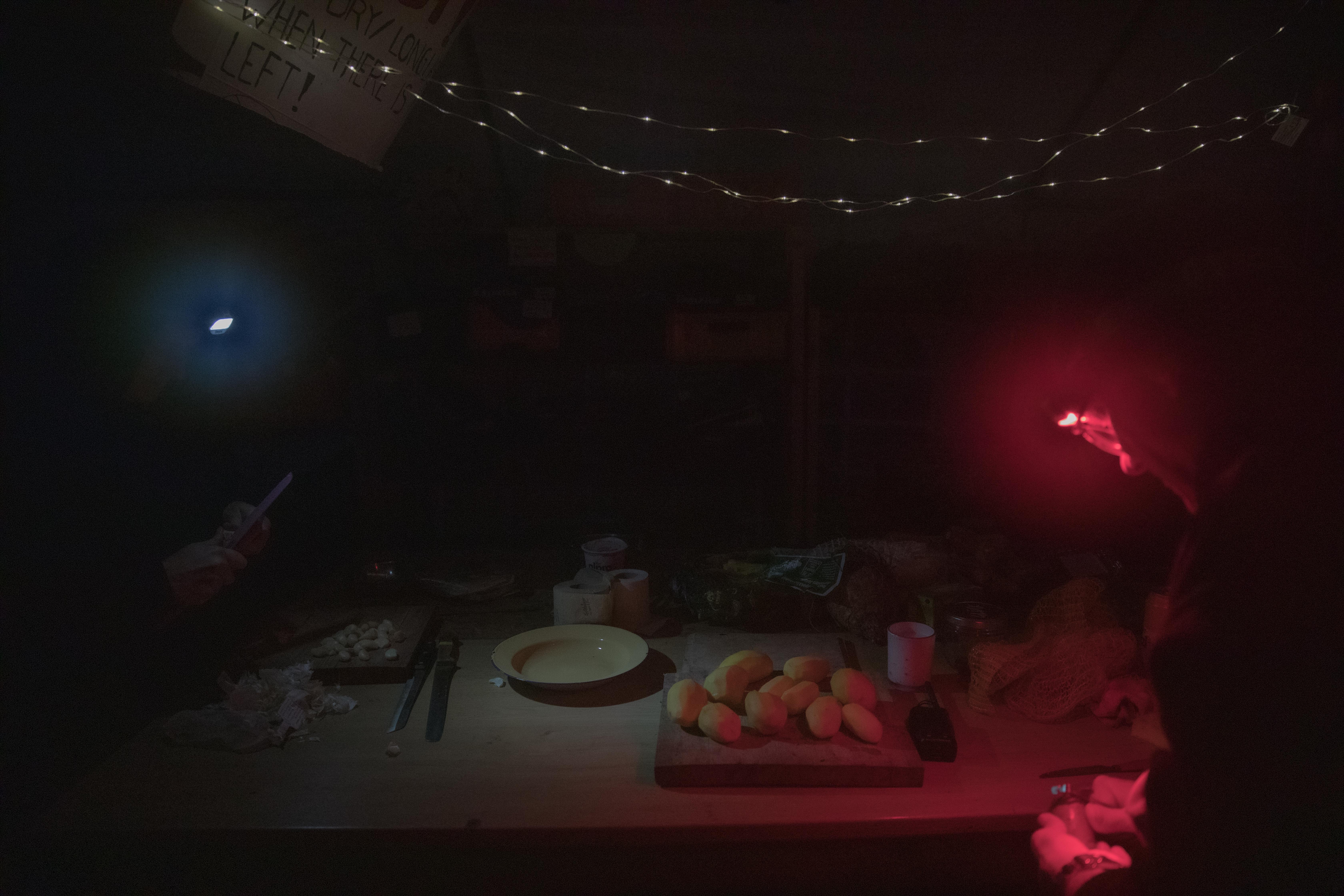 In the quiet of the night after the first day of the police evictions, two people move around a table illuminated by headlamps, preparing food for all those who pass through the camp