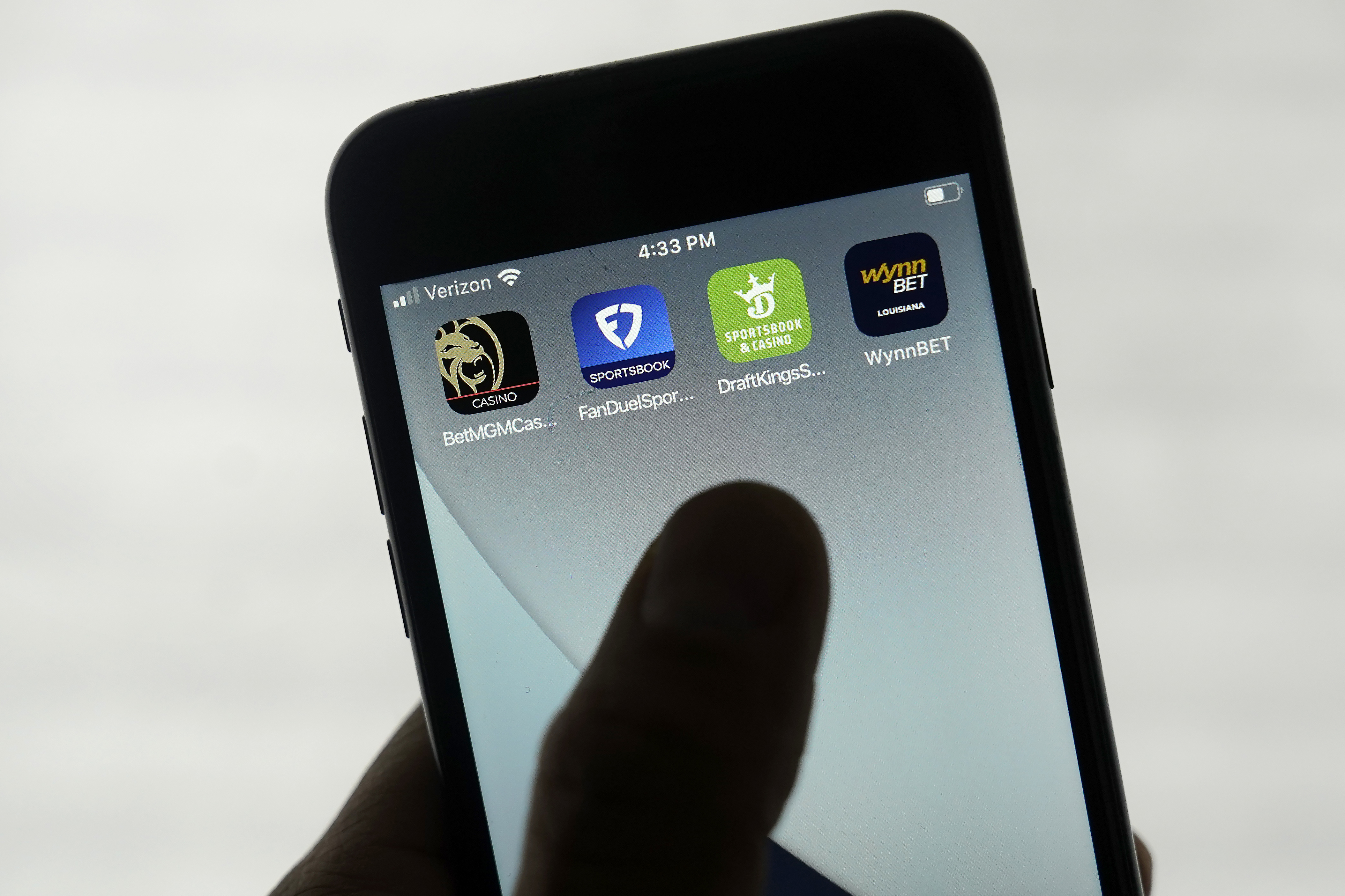 A shadowy hand touches a phone screen with gambling apps on it.