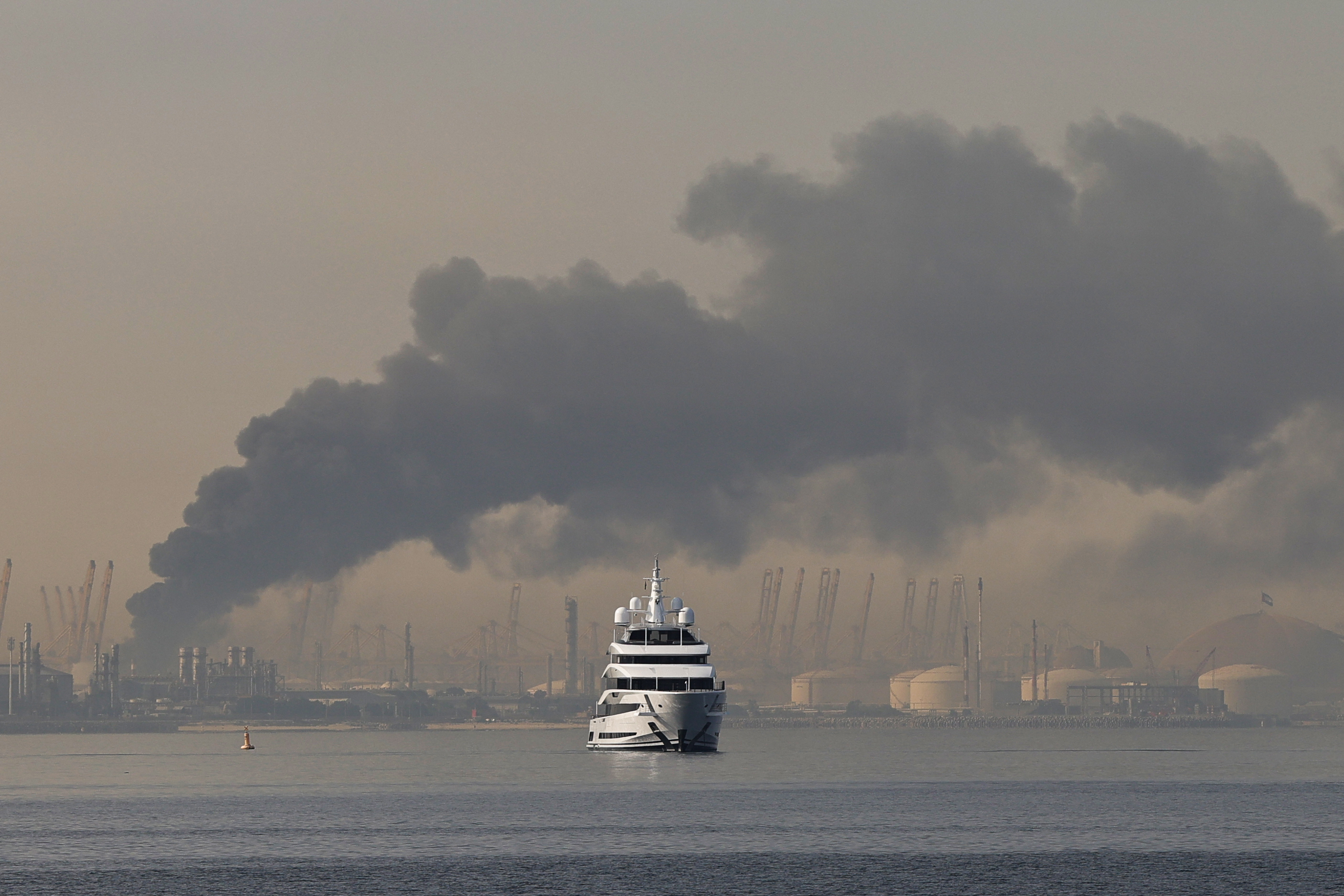 TOPSHOT - A yacht sails past a plume of smoke rising from the port of Jebel Ali following a reported Iranian strike in Dubai on March 1, 2026.