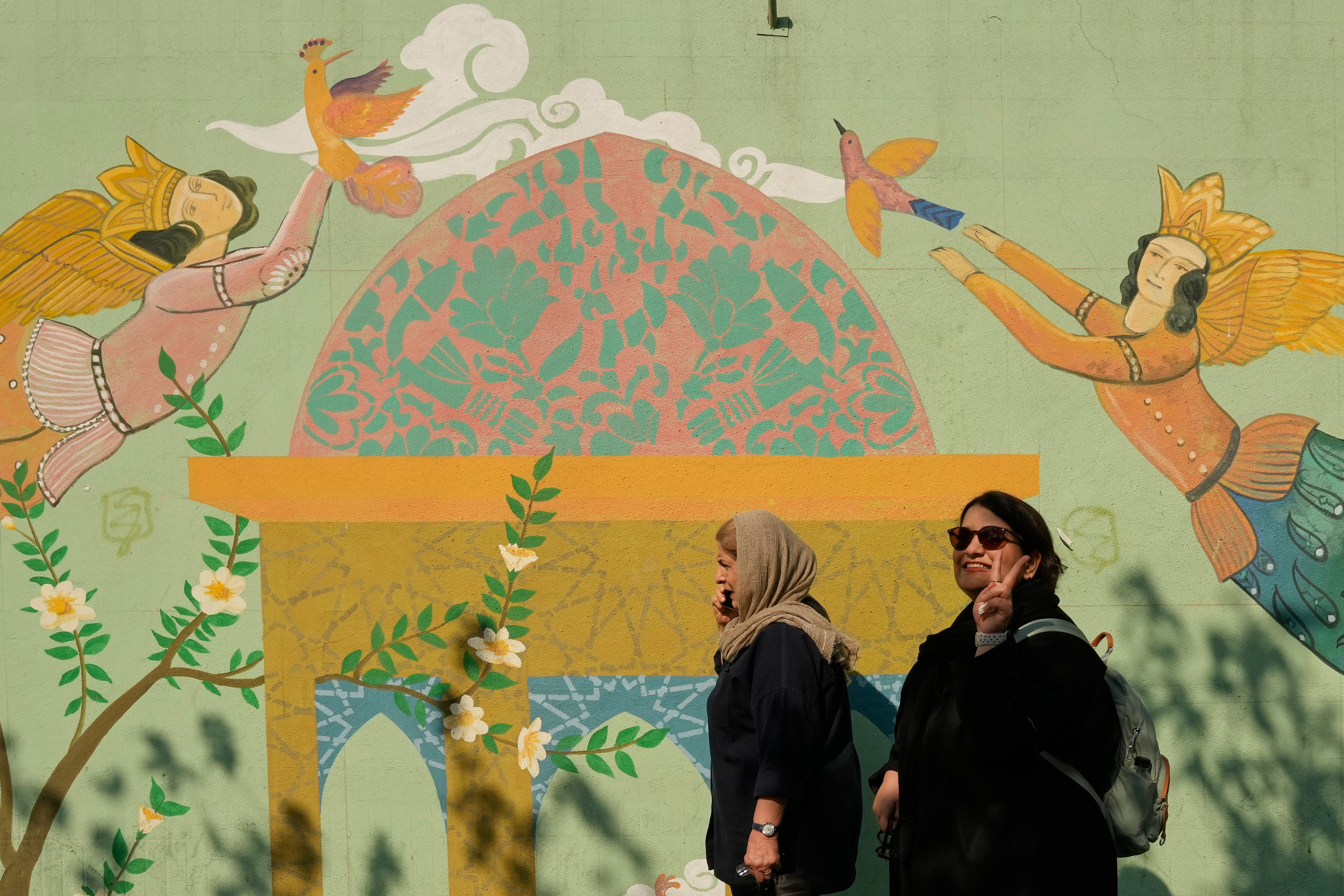 A woman flashes a victory sign as she walks past a painting on a wall at the Islamic Revolution street in Tehran, Iran, Monday, Oct. 26, 2026. (AP Photo/Vahid Salemi)