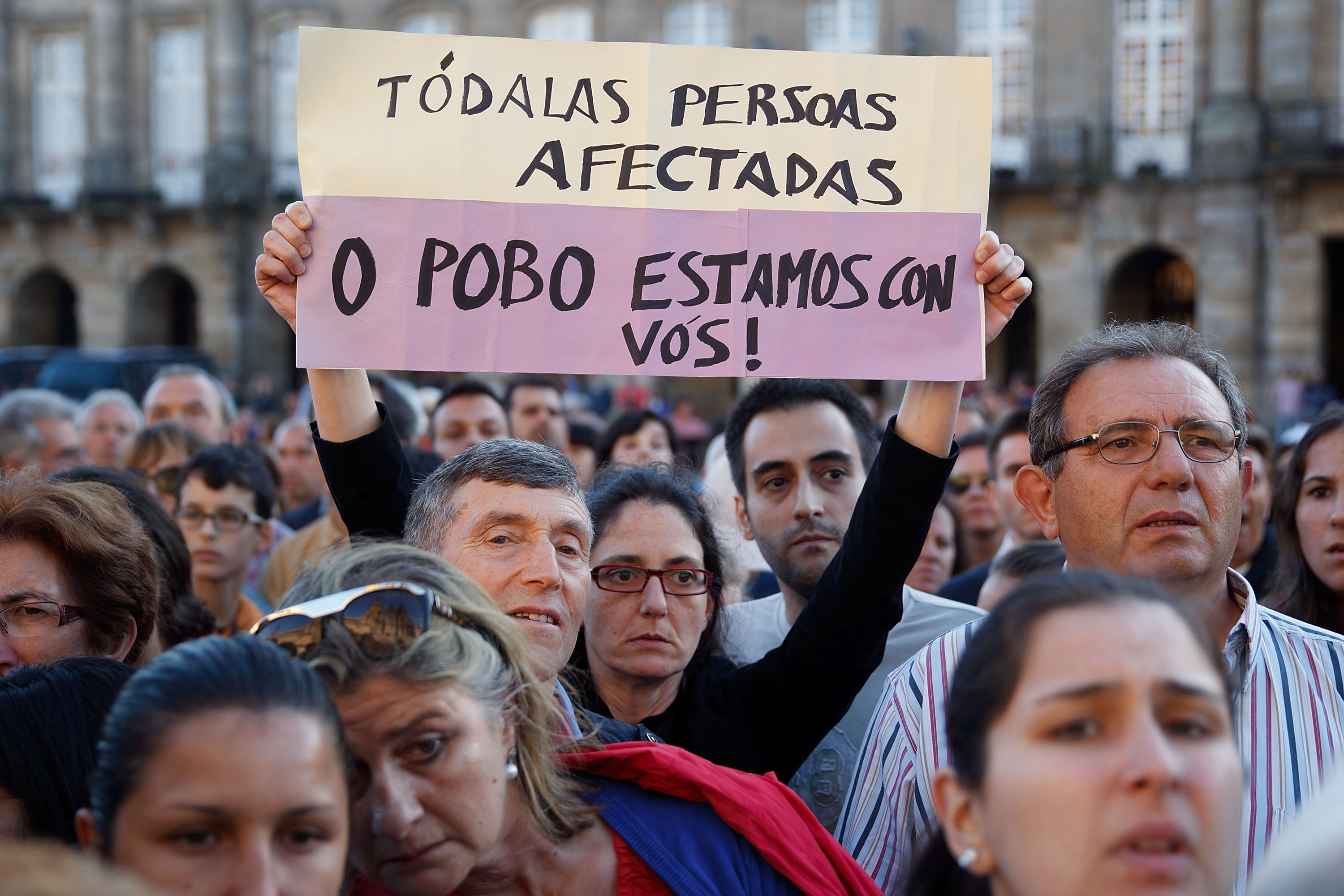 SANTIAGO DE COMPOSTELA, SPAIN - JULY 29: Santiago de Compostela people standing in Obradoiro Square, in front of Santiago de Compostela Cathedra, acknoweldge relatives of the victims with a sign that reads in gallego language: "Everyone afected. All the city is with you" after the memorial Mass for the vitims of the Spanish train crash on July 29, 2013 in Santiago de Compostela, Spain. The high speed train crashed after it derailed on a bend as it approached the north-western Spanish city of Santiago de Compostela at 8:40pm on July 24th, the eve of the Santiago de Compostela Festivities. At least 79 people have died and a further 130 are reported injured. The train driver, Garzon Amo, has been formally accused of reckless homicide and has been released with charges after attending to court. Ê(Photo by Gonzalo Arroyo Moreno/Getty Images)