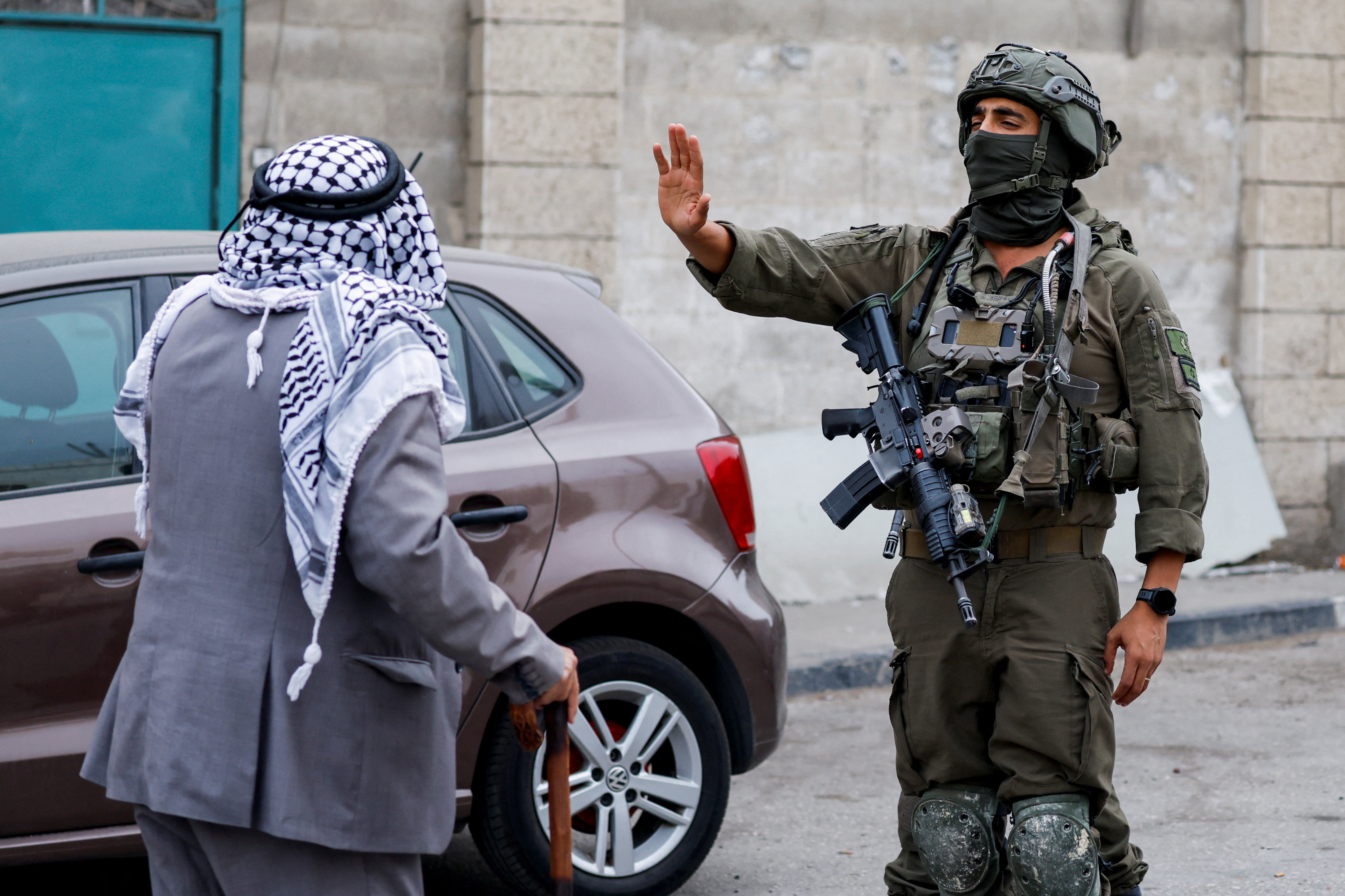 An Israeli soldier gestures towards a Palestinian man, forcing him to stop.